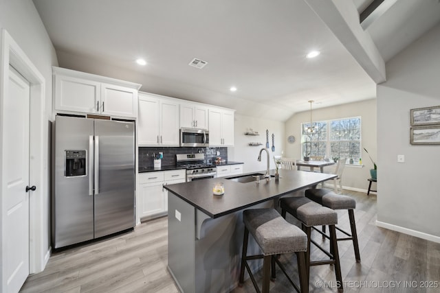 kitchen with decorative light fixtures, lofted ceiling, sink, white cabinets, and stainless steel appliances