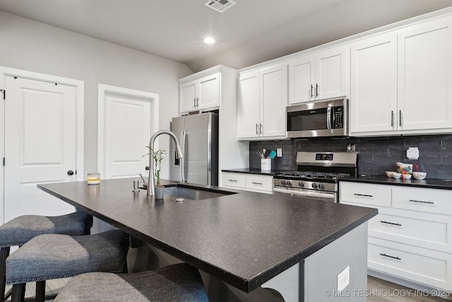 kitchen featuring sink, appliances with stainless steel finishes, a kitchen island with sink, a kitchen breakfast bar, and decorative backsplash