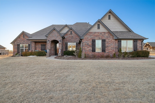 view of front of home featuring brick siding, a front lawn, and a shingled roof