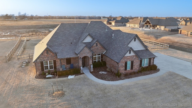 view of front facade with brick siding, a shingled roof, and fence