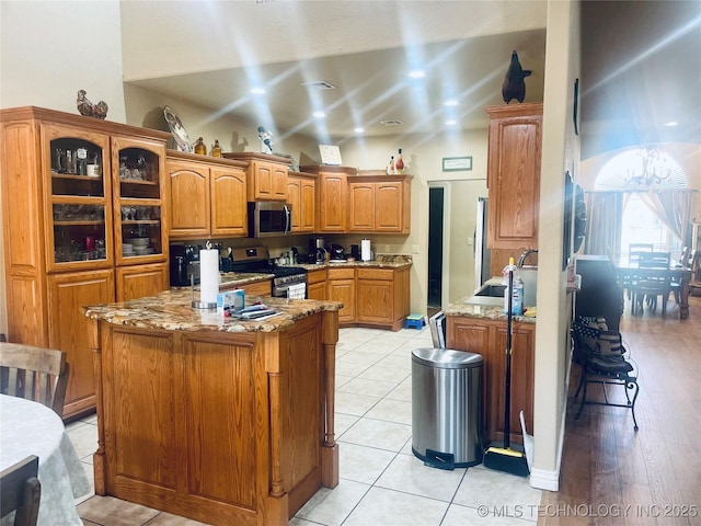 kitchen with light tile patterned floors, kitchen peninsula, a kitchen island, stainless steel appliances, and light stone countertops