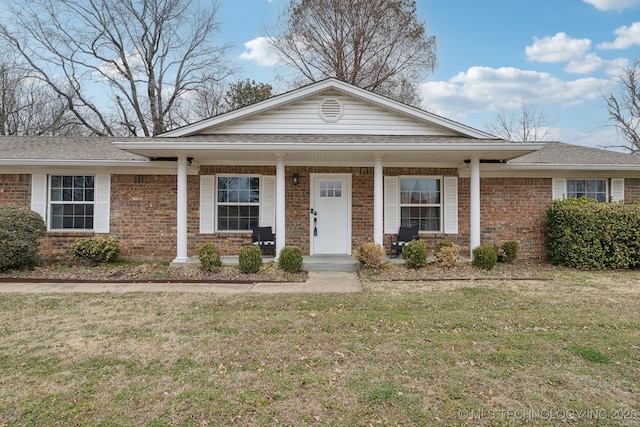 view of front of house featuring a front yard, a porch, brick siding, and roof with shingles