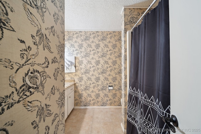 bathroom featuring tile patterned flooring, wallpapered walls, baseboards, vanity, and a textured ceiling