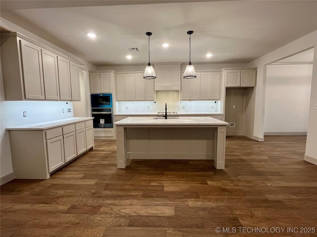 kitchen featuring hanging light fixtures, an island with sink, white cabinetry, and dark hardwood / wood-style flooring