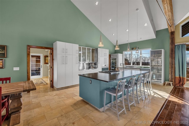 kitchen featuring a center island, high vaulted ceiling, hanging light fixtures, appliances with stainless steel finishes, and white cabinets