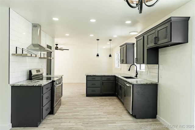 kitchen with wall chimney exhaust hood, sink, light stone counters, hanging light fixtures, and appliances with stainless steel finishes