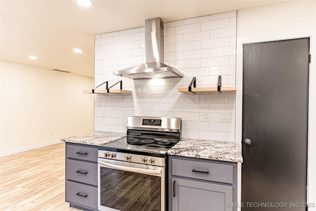 kitchen with wall chimney exhaust hood, tasteful backsplash, stainless steel range with electric stovetop, gray cabinets, and light stone countertops