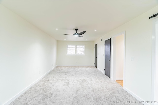 unfurnished room with light colored carpet, a barn door, and ceiling fan