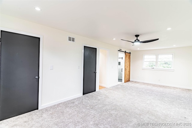unfurnished bedroom with a barn door, light colored carpet, and ceiling fan