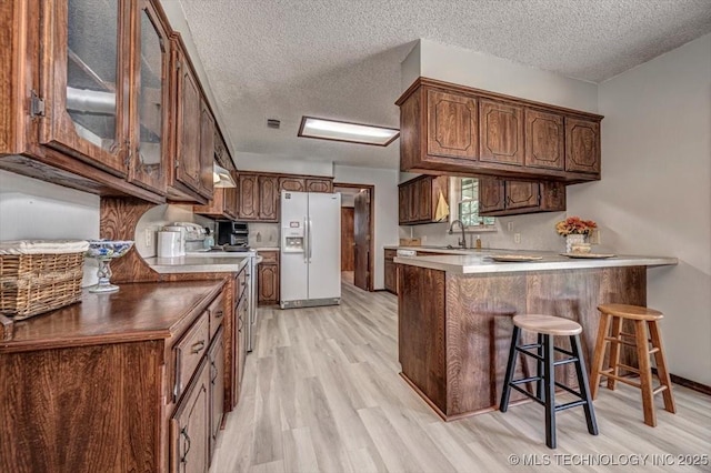 kitchen featuring a kitchen bar, white refrigerator with ice dispenser, kitchen peninsula, and a textured ceiling