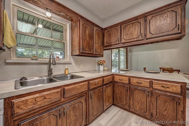 kitchen with sink, a textured ceiling, light hardwood / wood-style floors, and kitchen peninsula