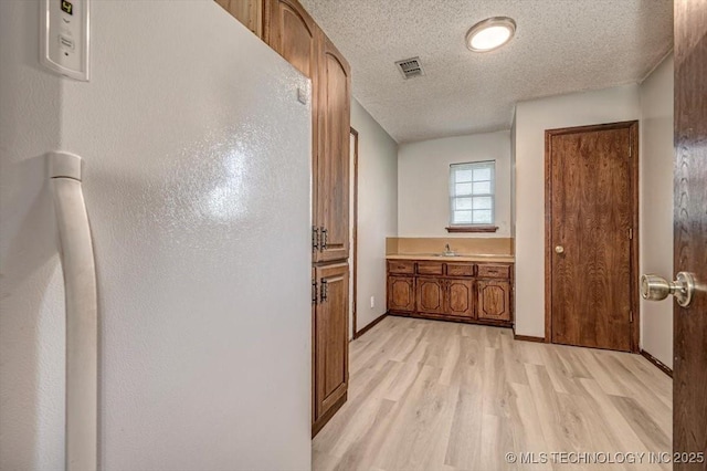 hallway with sink, light hardwood / wood-style floors, and a textured ceiling