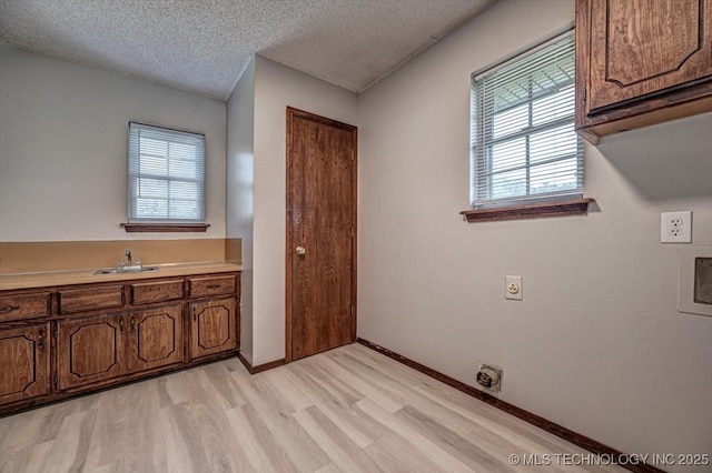 laundry area featuring sink, cabinets, a textured ceiling, light wood-type flooring, and electric dryer hookup