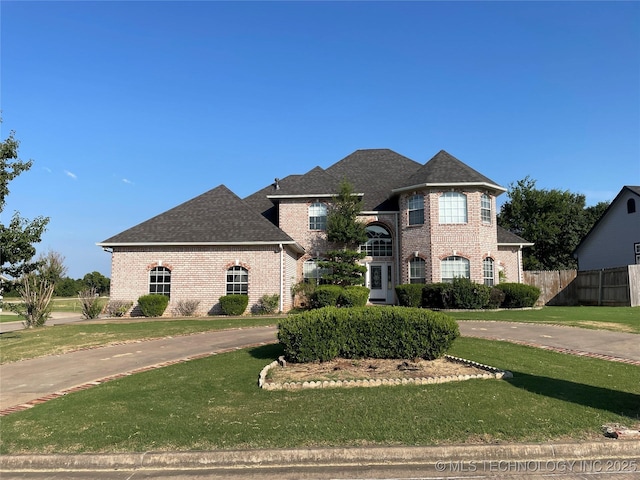 view of front of house with brick siding, a front lawn, a shingled roof, and fence