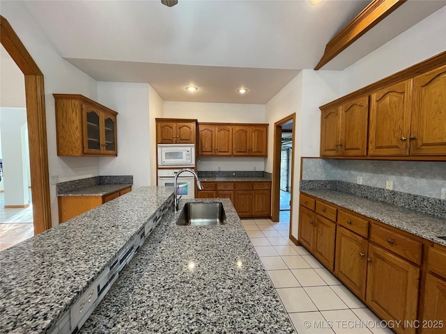 kitchen with glass insert cabinets, brown cabinets, a sink, and white microwave