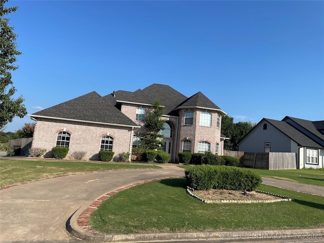 view of front of property featuring a shingled roof, brick siding, fence, and a front lawn