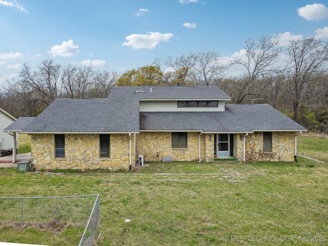 view of front of home with a front yard, roof with shingles, and stone siding