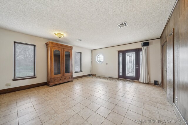 empty room with a textured ceiling, light tile patterned floors, baseboards, and visible vents