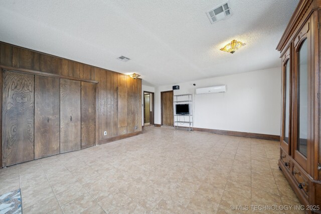 unfurnished living room with wooden walls, visible vents, baseboards, and a wall unit AC