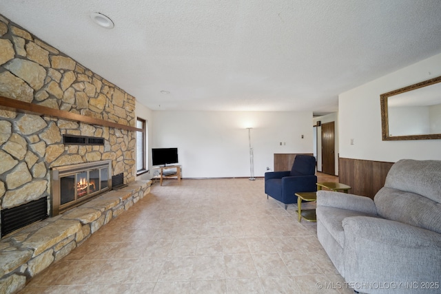 living room featuring wooden walls, a stone fireplace, wainscoting, and a textured ceiling