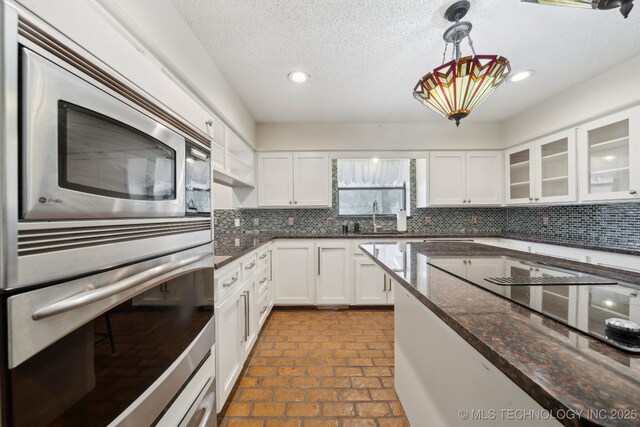 kitchen featuring glass insert cabinets, white cabinets, dark stone countertops, hanging light fixtures, and backsplash
