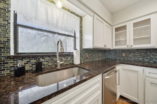 kitchen with a sink, decorative backsplash, white cabinetry, and dark stone countertops
