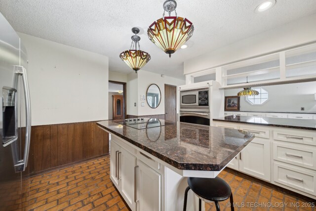 kitchen featuring a textured ceiling, a kitchen island, white cabinets, wainscoting, and stainless steel appliances