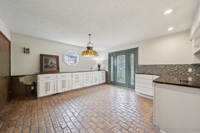 unfurnished dining area with a wainscoted wall, recessed lighting, brick floor, and a textured ceiling