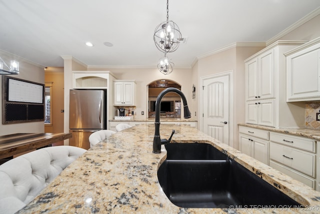 kitchen featuring pendant lighting, sink, stainless steel refrigerator, light stone countertops, and a chandelier