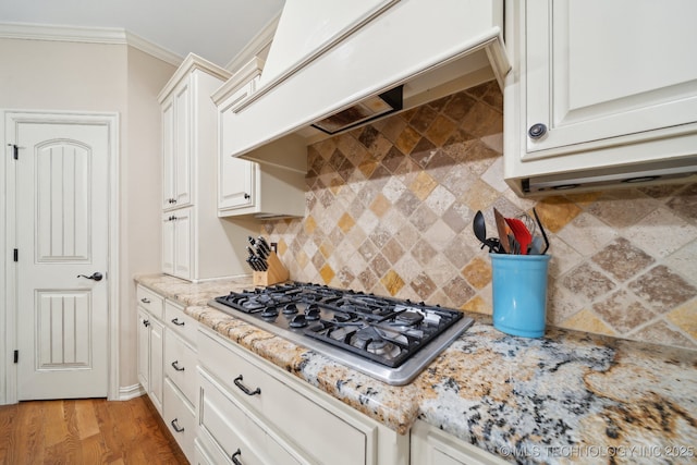 kitchen featuring white cabinets, stainless steel gas cooktop, light stone counters, crown molding, and custom range hood