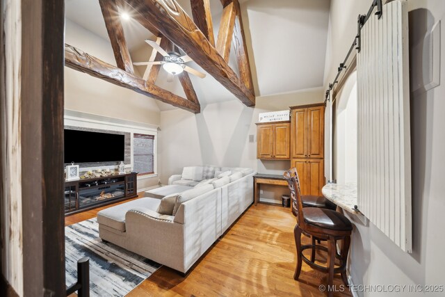 living room featuring vaulted ceiling with beams, ceiling fan, a barn door, and light wood-type flooring