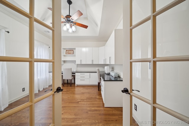 kitchen with built in desk, wood-type flooring, white cabinets, ceiling fan, and french doors