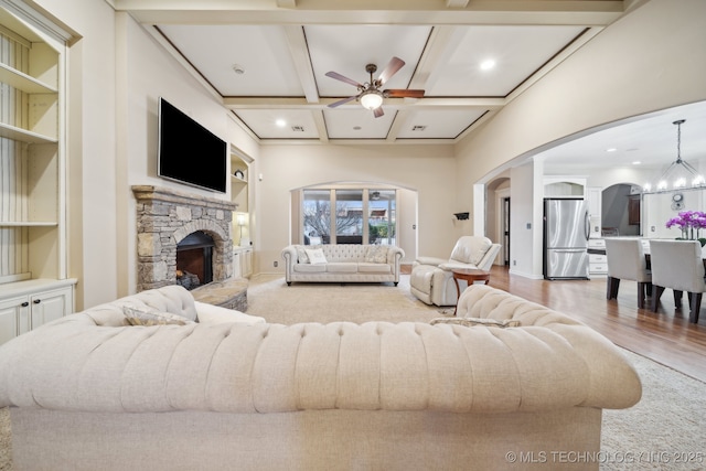 living room with coffered ceiling, wood-type flooring, beamed ceiling, a fireplace, and ceiling fan with notable chandelier