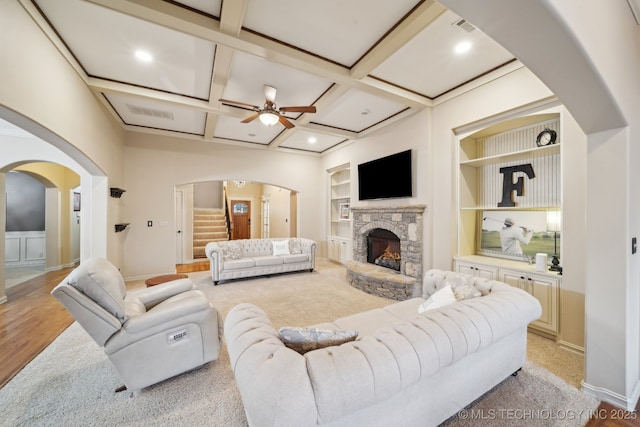 living room featuring a fireplace, beamed ceiling, coffered ceiling, ceiling fan, and built in shelves