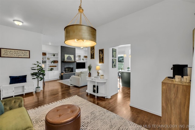 living room with dark wood-type flooring, a fireplace, and built in shelves