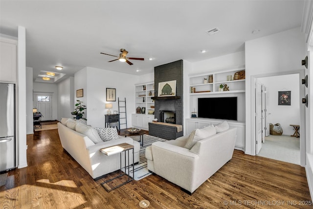 living room with ceiling fan, dark hardwood / wood-style flooring, a brick fireplace, and built in features