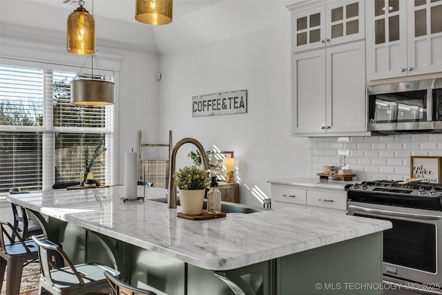 kitchen with pendant lighting, white cabinetry, stainless steel appliances, light stone countertops, and an island with sink