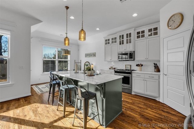 kitchen featuring pendant lighting, white cabinetry, stainless steel appliances, and a center island with sink