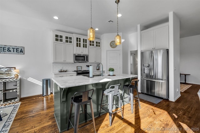 kitchen with a kitchen island with sink, white cabinetry, tasteful backsplash, and stainless steel appliances