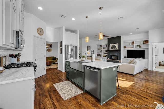 kitchen with sink, a center island with sink, pendant lighting, stainless steel appliances, and white cabinets