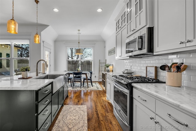 kitchen featuring sink, a kitchen island with sink, hanging light fixtures, stainless steel appliances, and dark hardwood / wood-style floors