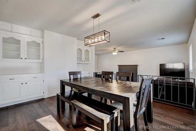 dining space with ceiling fan, dark hardwood / wood-style flooring, and a brick fireplace