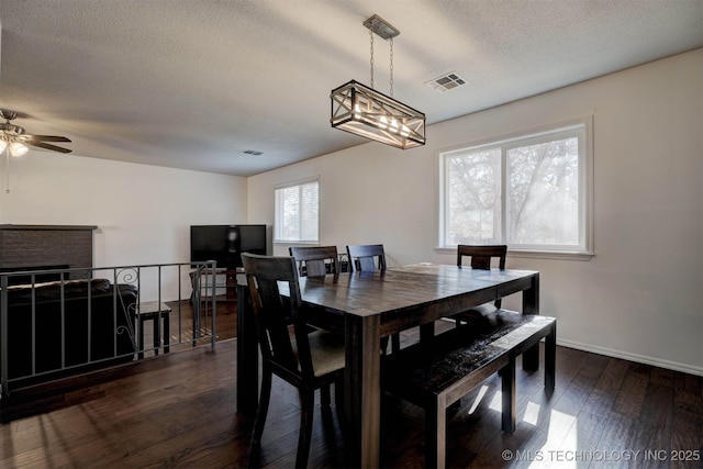 dining room featuring ceiling fan, dark hardwood / wood-style floors, a brick fireplace, and a textured ceiling