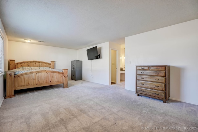 bedroom with ensuite bathroom, light carpet, and a textured ceiling