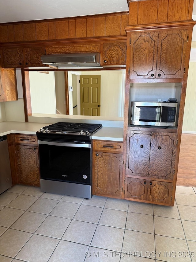 kitchen with light tile patterned flooring, appliances with stainless steel finishes, wall chimney range hood, and wood walls