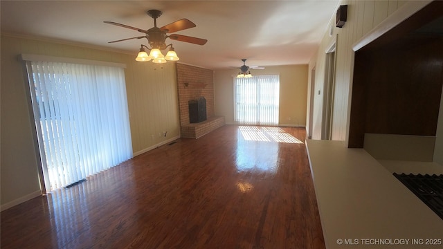 unfurnished living room with ceiling fan, a brick fireplace, crown molding, and dark hardwood / wood-style flooring