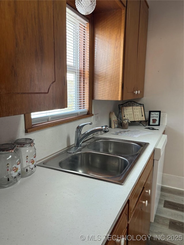 kitchen featuring light countertops, baseboards, white dishwasher, and a sink