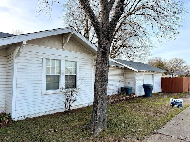 view of property exterior with central air condition unit, fence, a garage, and a lawn