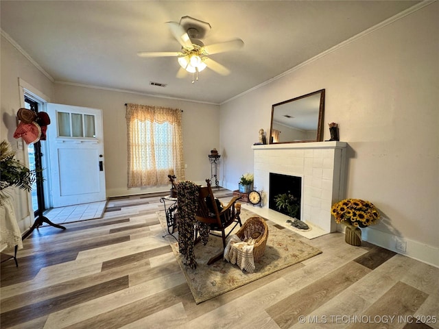 living room featuring a tile fireplace, ornamental molding, and light wood-type flooring