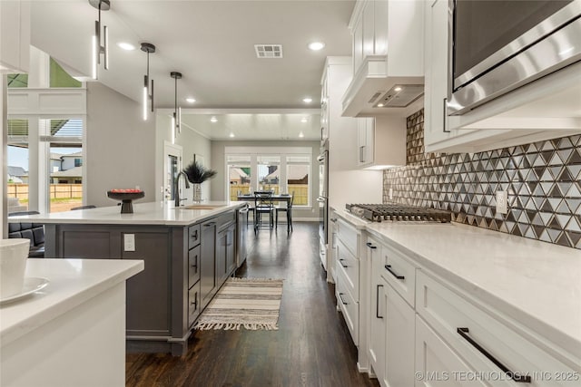 kitchen with dark wood-type flooring, sink, an island with sink, pendant lighting, and white cabinets